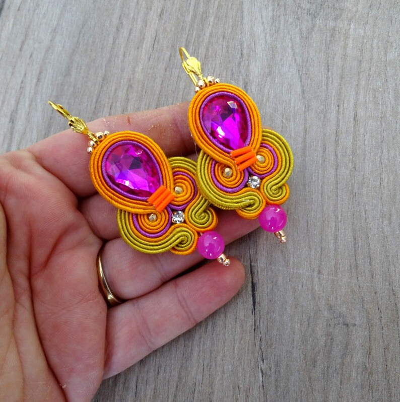May include: A pair of earrings with a pink and orange swirl design. The earrings feature a large pink crystal and a smaller pink bead.