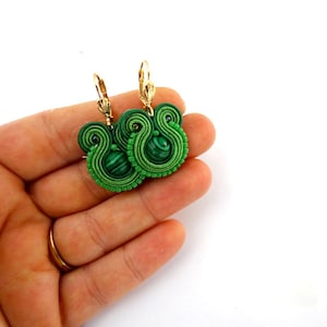May include: Green and gold earrings with a malachite stone in the centre. The earrings are made of a woven cord and have a dangling design.