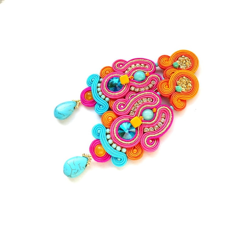 May include: A pair of colorful earrings with turquoise stones and a pink, orange, and blue design. The earrings are made with a technique called kumihimo, which involves braiding threads together to create intricate patterns.