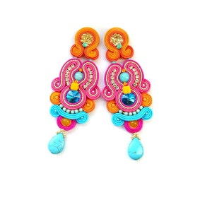 May include: A pair of long, colorful earrings with turquoise, pink, orange, and gold accents. The earrings have a unique, intricate design and feature a teardrop-shaped turquoise stone at the bottom.