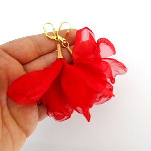 May include: A pair of red flower-shaped earrings with gold hooks. The earrings are made of fabric and have a delicate, feminine look.