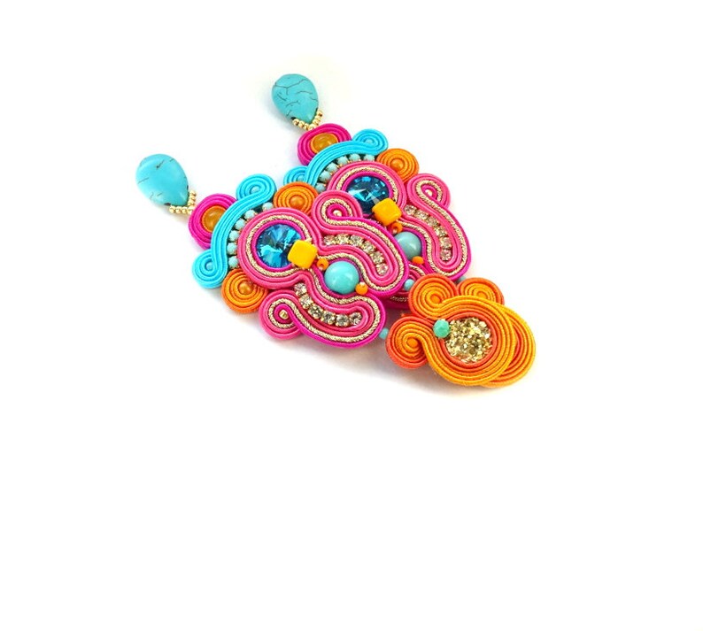 May include: A pair of colorful earrings with turquoise, orange, pink, and blue beads and rhinestones. The earrings are made of a woven cord material.