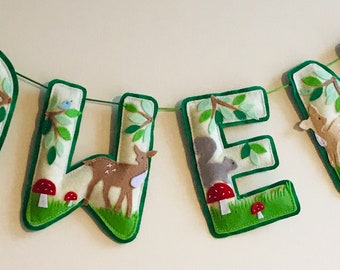 May include: A felt banner with the name "OWEN" spelled out in green letters. Each letter has a different woodland animal and foliage design.