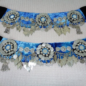Peut inclure: Deux ceintures en velours bleu avec des embellissements en pièces de monnaie argentées et un miroir au centre de chacune. Les ceintures ont des extrémités en velours noir.