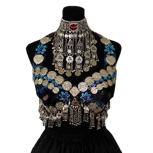 Könnte beinhalten: Ein dunkelblaues Samt-Neckholder-Top, verziert mit zahlreichen silberfarbenen runden Münzen, blauen Blumenakzenten und hängenden Metallanhängern. Eine passende, verzierte silberfarbene Halskette mit roten und blauen Steineinlagen.