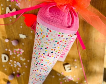 May include: A pink and white cone-shaped party favor with colorful polka dots and a pink tulle bow. The cone is decorated with the name "Daria".