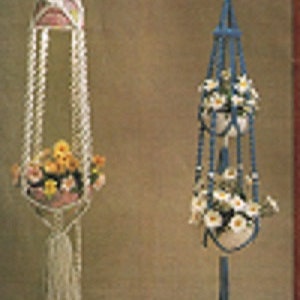 May include: Two macrame plant hangers, one white and one blue, with white flowers in the pots.