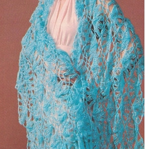 May include: A woman wearing a light blue crocheted shawl with fringe. The shawl has a delicate lace pattern. The model is wearing a pink blouse and the shawl is draped over her shoulders. The image includes the text "2310-215".