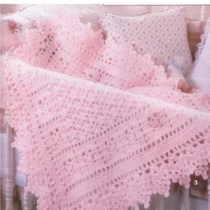 May include: A pale pink crocheted baby blanket with a decorative scalloped edge, draped over a cot. The blanket has an openwork design with floral details. A floral patterned pillow is in the background.