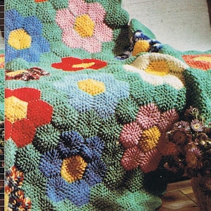 May include: A crocheted blanket with a scalloped edge featuring a repeating pattern of colorful flowers. The blanket is made with a variety of colors, including green, blue, pink, red, yellow, and white.