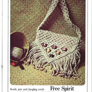 Puede incluir: Un bolso de macramé beige con flecos y cuentas de madera. El bolso tiene una correa larga y está hecho de fibra natural. "Free Spirit" está escrito en la imagen.