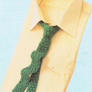 Op de afbeelding: Een geel overhemd met een groene gecrochete das. De das is geknoopt en hangt aan de voorkant van het overhemd.