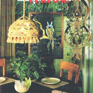 May include: A book cover with the title "MACRAMÉ with a PURPOSE" in red text. The cover features a macrame lampshade hanging from the ceiling, a macrame plant hanger, and a stained glass window with a bird design. The text "Instructions for 15 projects" is at the bottom of the cover.