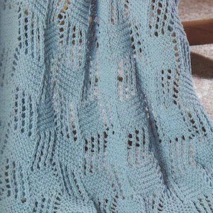 Könnte beinhalten: Eine hellblaue gehäkelte Decke mit einem Spitzenmuster. Die Decke ist aus weichem Garn gefertigt und hat ein zartes, luftiges Gefühl.