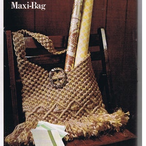 May include: A brown crocheted bag with a fringe border and a metal buckle. The bag is filled with rolled up wrapping paper and is sitting on a wooden chair. The text "Maxi-Bag" is printed at the top of the image.