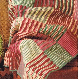 Op de afbeelding: Een gehaakt deken met een patchwork ontwerp in tinten roze, groen en wit.