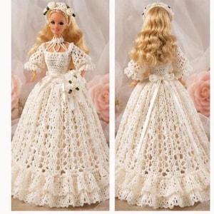 May include: A blonde doll wearing a white crocheted wedding gown with a full skirt, ruffled hem, and puff sleeves. The doll features a matching crocheted headpiece with small white flowers and a white ribbon tied at the waist of the dress.