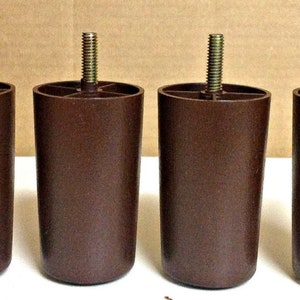 May include: Four brown furniture legs with threaded metal studs. The legs are cylindrical with a slightly tapered shape and are designed for easy attachment to furniture. They are made of a durable plastic material.