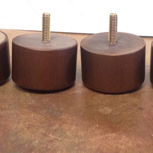 May include: Four brown wooden furniture legs with a threaded metal screw in the center of each. The legs are approximately 3 inches tall.