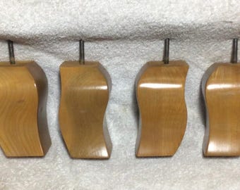 Könnte beinhalten: Vier Holzmöbelfüße mit hellbraunem Finish. Jeder Fuß hat ein geschwungenes Design und eine Metallstange, die sich von oben erstreckt. Diese Füße sind wahrscheinlich für einen Stuhl oder ein Sofa.