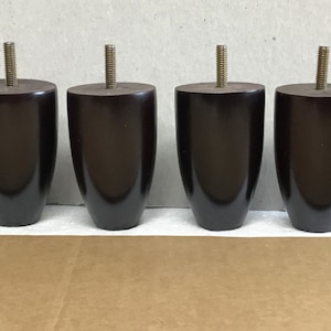 May include: Four dark brown wooden furniture legs with a threaded metal insert on top. The legs are shaped like a rounded oval.