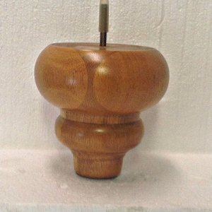 May include: A wooden furniture leg with a rounded top and a threaded metal insert. The leg is a light brown color and has a smooth finish.