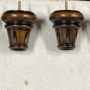 May include: Set of four brown wooden furniture legs with a decorative design. Each leg has a threaded metal screw for attaching to furniture.