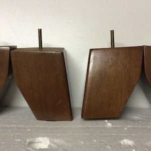 May include: Four brown wooden furniture legs with a metal screw in the top of each leg.