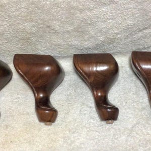 May include: Four wooden furniture legs with a dark brown finish. Each leg has a curved design and a rounded foot. The legs are likely for a sofa, chair, or other furniture piece.