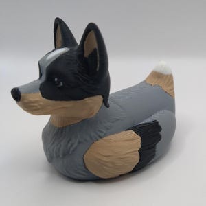 May include: A blue and black rubber duck with a white spot on its tail, shaped like an Australian Shepherd dog.