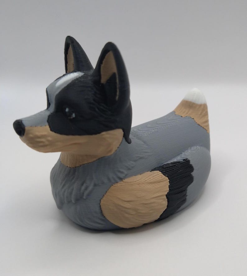 May include: A blue and black rubber duck with a white spot on its tail, shaped like an Australian Shepherd dog.