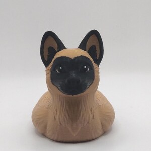 May include: A 3D-printed figurine of a dog, featuring a tan body and black markings around the eyes, ears, and nose. The dog has a friendly expression and is set against a plain white background. The figurine is a decorative item.