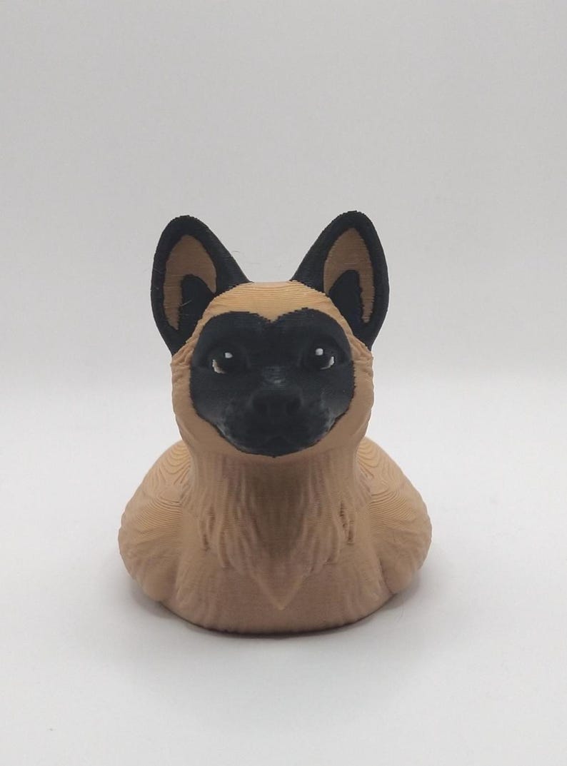 May include: A 3D-printed figurine of a dog, featuring a tan body and black markings around the eyes, ears, and nose. The dog has a friendly expression and is set against a plain white background. The figurine is a decorative item.