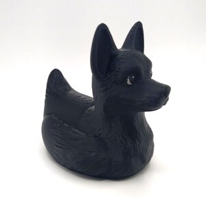 May include: A black rubber duck shaped like a dog. The duck has pointed ears, a long snout, and a textured surface. The dog-shaped duck is a unique and playful bath toy.