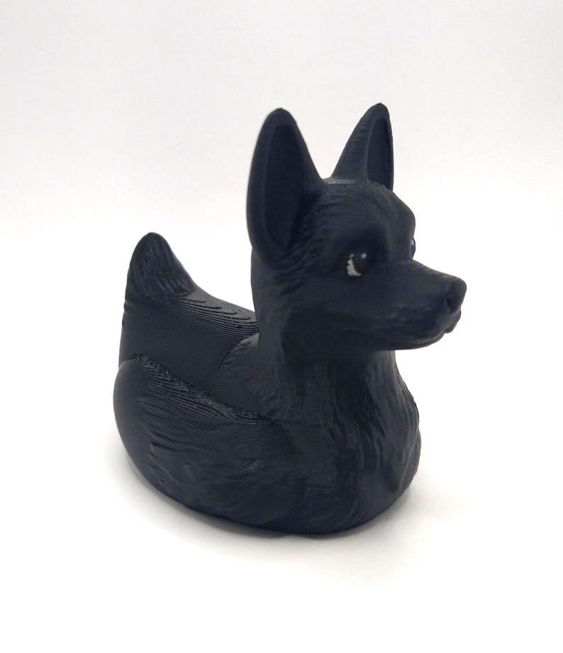 May include: A black rubber duck shaped like a dog. The duck has pointed ears, a long snout, and a textured surface. The dog-shaped duck is a unique and playful bath toy.