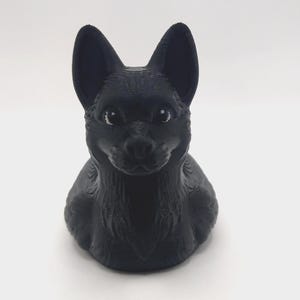 May include: A black 3D-printed figurine of a dog, featuring upright ears and a detailed textured surface. The dog is depicted in a seated position, with a focused expression.