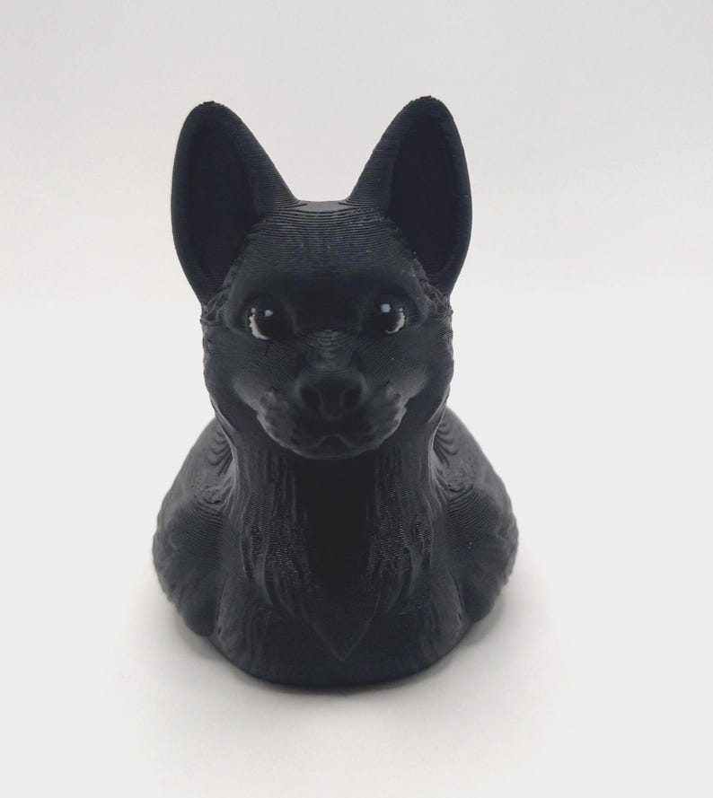 May include: A black 3D-printed figurine of a dog, featuring upright ears and a detailed textured surface. The dog is depicted in a seated position, with a focused expression.