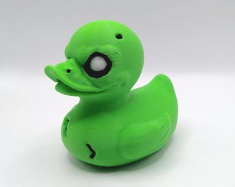 May include: A green rubber duck with a single white eye and a black pupil. The duck has a small hole on the top of its head.