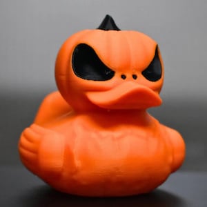 May include: Orange rubber duck shaped like a pumpkin with black eyes and a pointy stem.