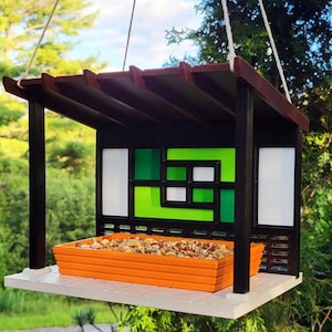 May include: A bird feeder with a brown wooden roof and a green and white stained glass design. The feeder has a tray for birdseed and is hanging from a string.