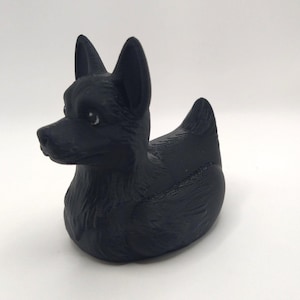 May include: A black dog-shaped figurine with upright ears and a rounded body. The figurine has a smooth, matte finish and is set against a plain white background. The dog's features are detailed, with visible eyes and a defined snout.