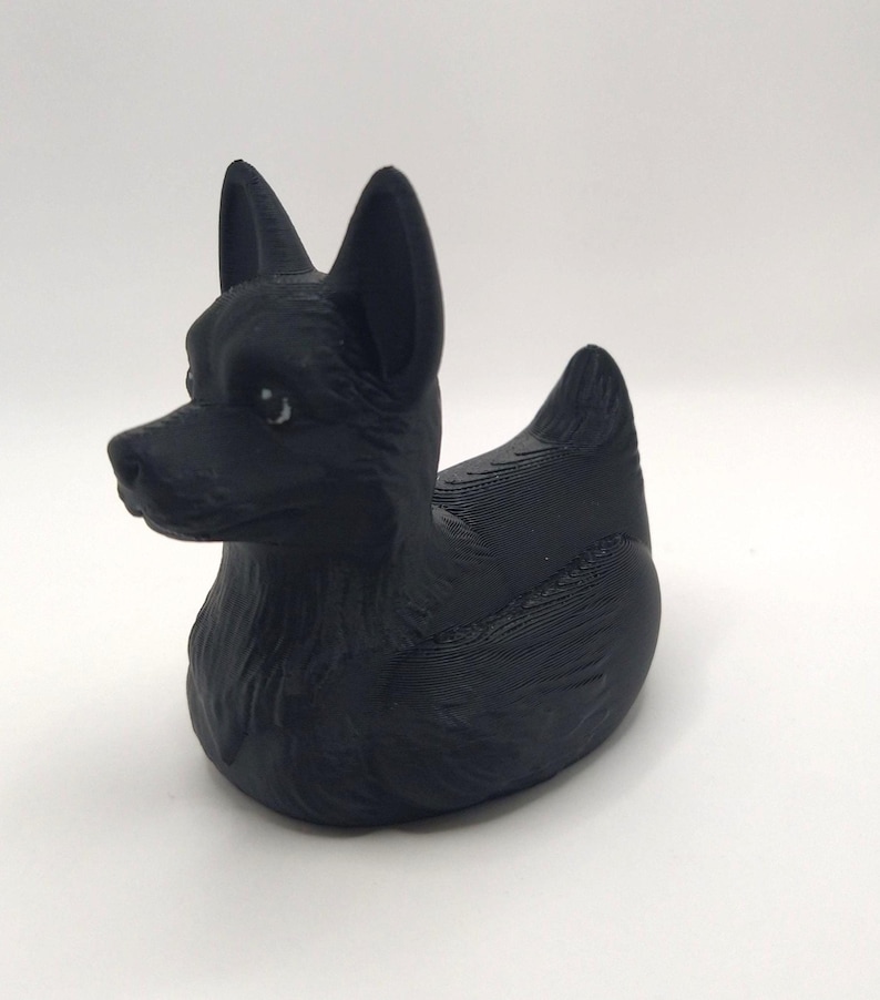 May include: A black dog-shaped figurine with upright ears and a rounded body. The figurine has a smooth, matte finish and is set against a plain white background. The dog's features are detailed, with visible eyes and a defined snout.