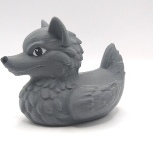 May include: A gray rubber duck with a wolf head and a detailed, textured design. The duck has a fierce expression and black eyes.