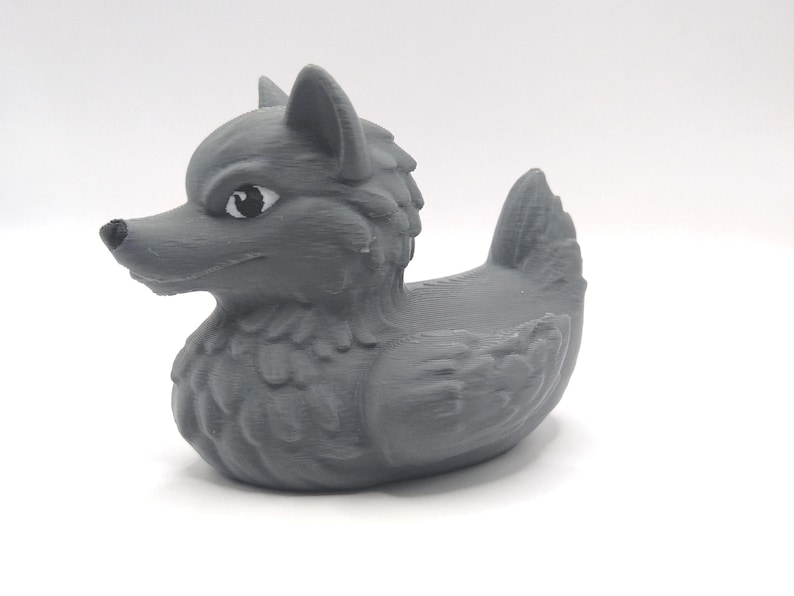May include: A gray rubber duck with a wolf head and a detailed, textured design. The duck has a fierce expression and black eyes.