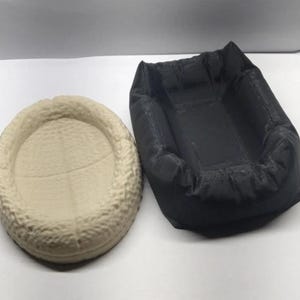 Op de afbeelding: Twee kleine, ronde, getextureerde bedden voor kleine huisdieren. Een bed is beige en de andere is zwart.