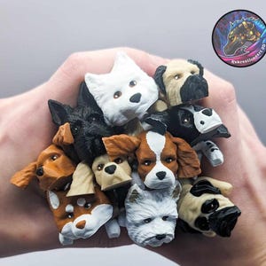 May include: A collection of 12 small, hand-painted dog head figurines. The figurines are made of a light brown, white, and black material. They are all different breeds of dogs, including a pug, a bulldog, a terrier, and a spaniel.