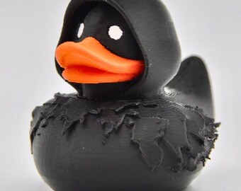 May include: A black rubber duck wearing a black hooded robe. The duck has an orange beak and white eyes.