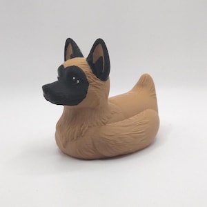 May include: A rubber duck toy designed to resemble a dog. The duck has a tan body with black accents on the ears, snout, and eyes. The toy is a novelty item, likely for bath time or as a decorative piece.