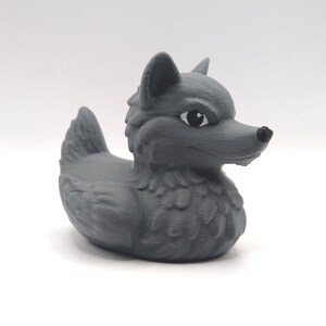 May include: A gray rubber duck with a wolf head and black eyes. The duck has a textured surface and is designed to float in water.