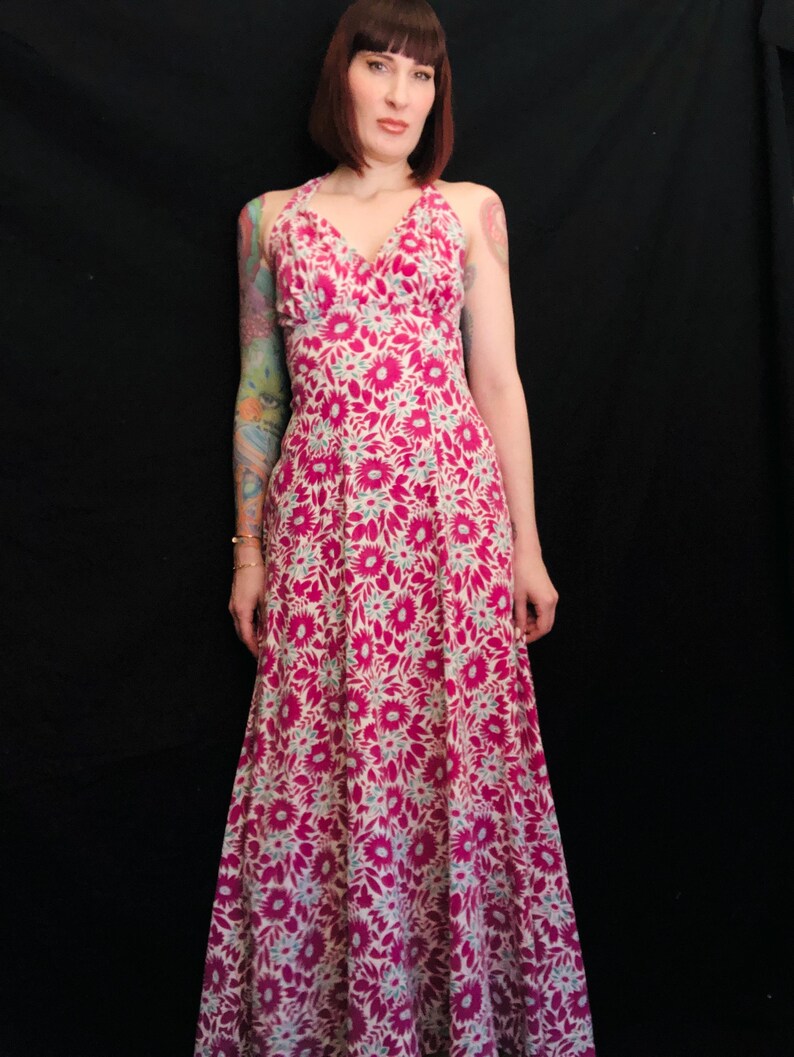 May include: A long, pink and white floral print maxi dress with a halter neckline. The dress has a fitted bodice and a flowing skirt.